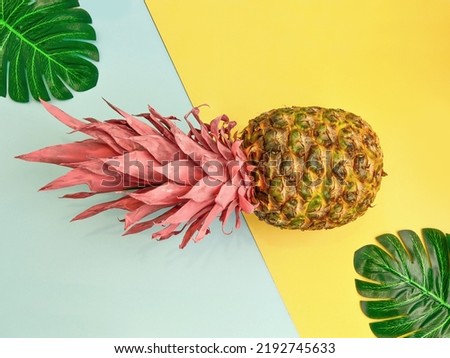 Creative summer layout made of pineapple with pink leaves and tropical leaves against blue and yellow background. Original pineapple decoration. Creative summer idea.  Fruit concept. Copy space.