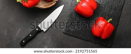Fresh red bell pepper with knife on dark background, top view