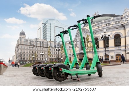 Many modern green electric scooters sharing parked city street. Self-service street transport rental service. Rent urban mobility vehicle with smartphone application. Zero emission green eco energy Royalty-Free Stock Photo #2192753637