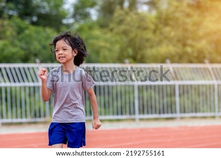 Portrait Asian Thai girl, aged 4 to 6 years old, looks cute and cheerful. She was jogging in an outdoor sports field. happily and joyfully Running and playing exercises make your body fit and healthy