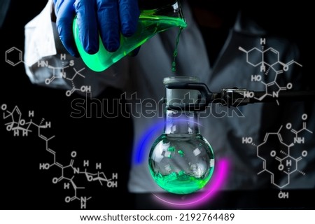 A woman scientist experimenting with a green fluorescent solution in a glass round bottom flask in dark chemistry laboratory for health care medicine development. Copy space black background Royalty-Free Stock Photo #2192764489