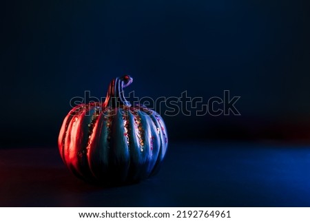 Decorative pumpkin with orange sparkles in neon red and blue light on the dark. Halloween decor and background with copy space. Selective focus.