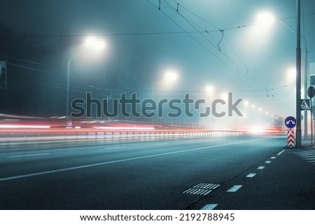 View empty dark night blue foggy misty rainy highway city road backlight red traces low poor visibility cold spring autumn season. Seasonal bad rainy weather accident danger warning car fog light Royalty-Free Stock Photo #2192788945