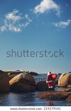 Santa Claus out of context on a beach looking at the view of the ocean with copyspace