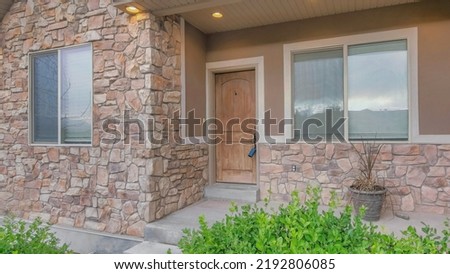 Panorama Whispy white clouds Exterior of a house with stone veneer wall and wooden door with lockbox. There is a concrete entrance in the middle of the shrubs at the front of a porch Royalty-Free Stock Photo #2192806085