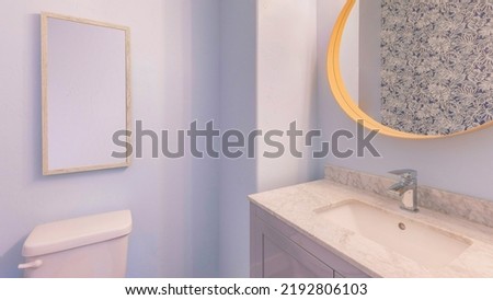 Panorama Powder blue bathroom interior with floral wall paper. There is a toilet with portrait picture frame at the back and a vanity sink with marble counter and framed oval mirror.