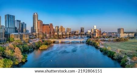 Colorado River near the district urban area of Austin, Texas. There are bridges over the river and a view of skyscraper buildings on the left and large field at the right side against the sunset sky. Royalty-Free Stock Photo #2192806151