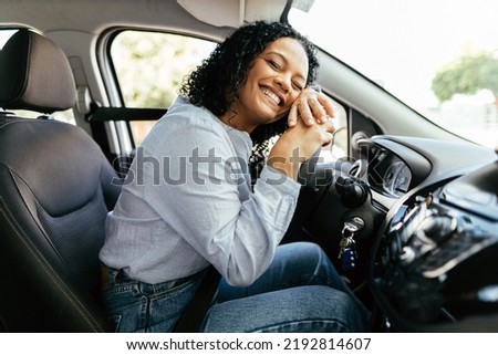 Young and cheerful woman enjoying new car hugging steering wheel sitting inside. Woman driving a new car.