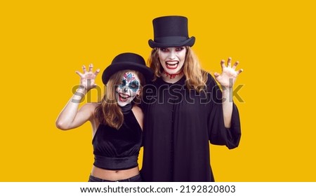 Mother and child having fun on Halloween. Studio portrait mum and daughter in spooky costumes. Beautiful vampire woman and little girl with Catrina make up look at camera isolated on yellow