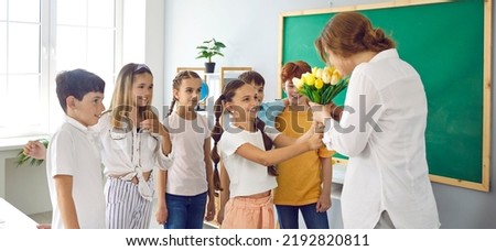 Cute schoolchildren with flowers for their best female teacher at school in honor of holiday. Preteen classmates in classroom give teacher bouquet of tulips. Teacher's day concept. Web banner. Royalty-Free Stock Photo #2192820811