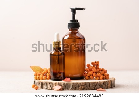 Set of beauty cosmetics on podium from saw cut tree with autumn leaves and rowan berries. Autumn concept of skincare, fall sales, Thanksgiving cosmetic gifts
