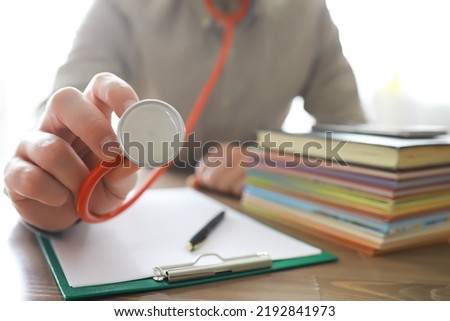 Male doctor in white lab coat reading text book, search information and working on laptop computer with  medical stethoscope on the desk in room at clinic. Medical knowledge and education concept.
