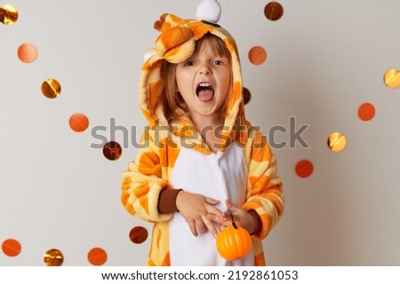 Emotional little girl in giraffe costume holding pumpkin candlestick at home. Halloween party