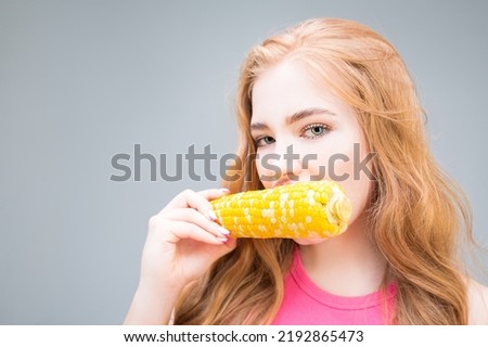 Young beautiful woman eating corn isolated on gray background. Healthy eating concept. Diet.