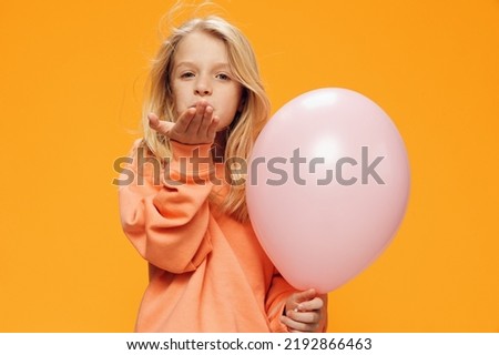 a cute, beautiful school-age girl stands on a bright background with a balloon and sends an air kiss to the camera. Horizontal photo with empty space for advertising layout