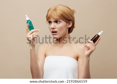 A nice woman in a towel with clean white skin, red hair pinned back hair on a beige background with two new facial serums takes care of the skin.Horizontal studio shot.