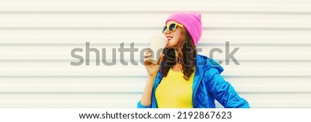 Portrait of stylish happy smiling young woman with cup of coffee wearing colorful pink hat, blue jacket on white background