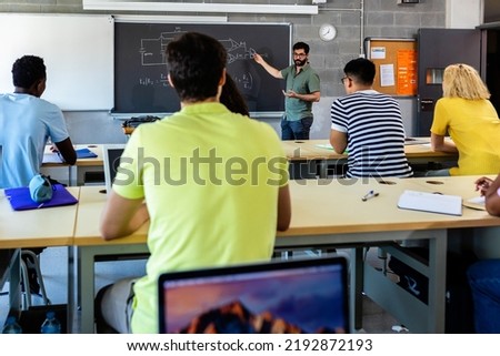 Young adult male lecturer teaching during technology class. Multiracial young students listening teacher in classroom Royalty-Free Stock Photo #2192872193