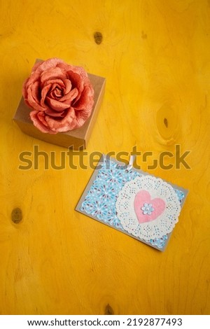 Blue postcard with pink heart, box and fabric rose flower on bright yellow background. Valentines day, birthday present. Top view, copy space, vertical