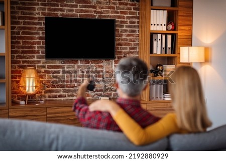 Adult caucasian man with remote control and lady relaxing, watching tv with blank screen and enjoy free time in living room interior. Couple and movie night at home together, entertainment with Royalty-Free Stock Photo #2192880929