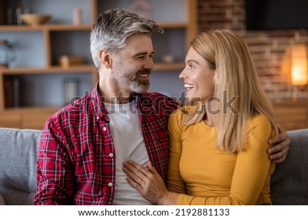 Cheerful middle aged caucasian husband with beard and woman look at each other, talk, enjoy free time in living room interior. Love, couple relationship, romance and family at home during covid-19 Royalty-Free Stock Photo #2192881133