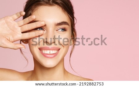 Skin care. Woman with beauty face touching healthy facial skin portrait. Beautiful smiling girl model with natural makeup touching glowing hydrated skin on pink background closeup