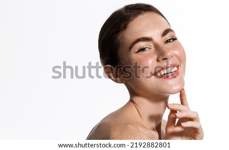 Skin care and women beauty. Girl with glowing healthy skin, touching her face and gazing at camera, standing with bare shoulders, perfect body without blemishes, white background