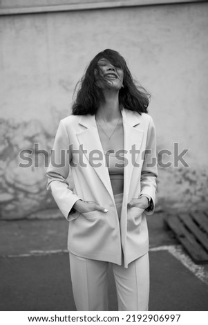 Portrait of beautiful modern woman in parking area. Fashionable. White suit. Crop top. Black hair. Slim and tall. Daily life. Work and leisure. City background. Black and white photo Royalty-Free Stock Photo #2192906997