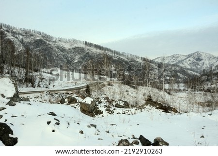 An asphalt road going through a snow-covered valley surrounded by high mountains in winter. Altai, Siberia, Russia.
