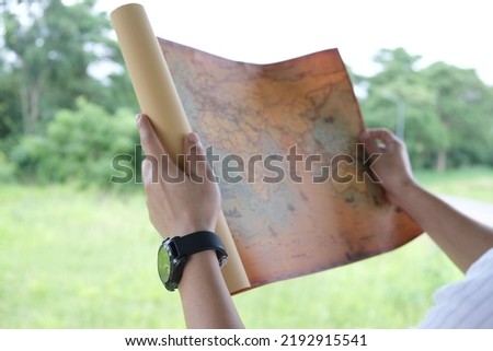 young man's hand holding a map travel to study travel routes around the world background Picture of trees on a lush green hill