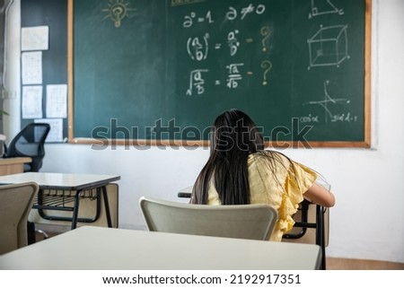 Education. Back view of school girl on lesson in classroom write hardworking on blackboard, primary child is sitting lessons at table in school writing or drawing in notebook, Back to school concept Royalty-Free Stock Photo #2192917351