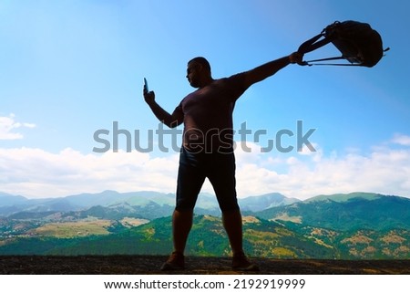 silhouette of tourist man stand of hill mountains at blue cloud sky background. looking direction in navigation map. nature background. mobile cell phone and rucksack in hands. male backpacker.