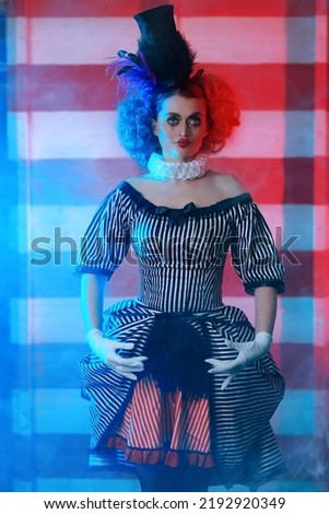Circus performer girl in a clown costume performs a knife throwing trick. The dark circus concept. Retro style. Royalty-Free Stock Photo #2192920349