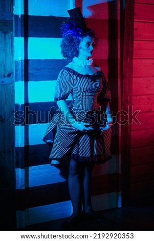 The dark circus concept. Circus performer in a clown costume performs a knife throwing trick. Retro style. Royalty-Free Stock Photo #2192920353