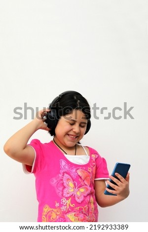 10-year-old Hispanic girl listens to music on her headphones connected to her cell phone dances, sings and enjoys the rhythm happy and excited
