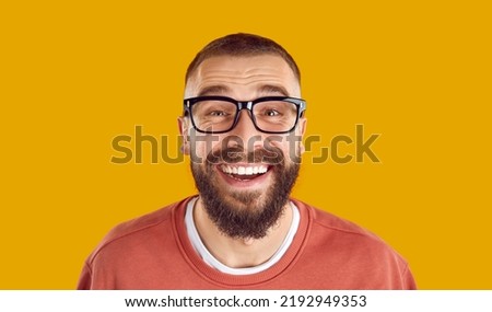 Studio portrait of happy man in glasses. Closeup headshot of cheerful funny bearded nerdy young man wearing eyeglasses looking at camera, smiling and laughing isolated on yellow orange background