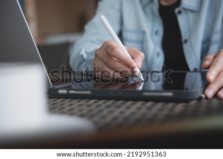 Business woman using stylus pen signing on digital tablet and working on laptop computer at office, close up. Woman freelancer, graphic designer online working at coffee shop