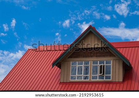 Red roof with dormer in the blue sky background. Decorative metal roof. Types of roof roofs.The roof of the house from a metal profile. Roofing. Stainless steel cladding. Nobody, copyspace for text Royalty-Free Stock Photo #2192953615