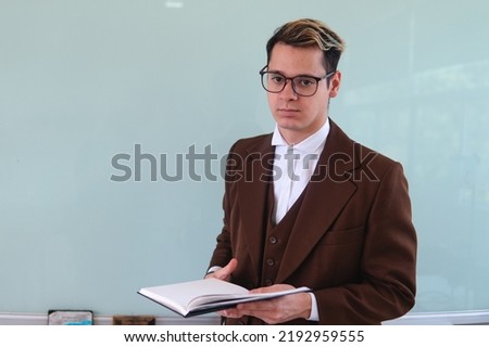 Teacher in front of the class explaining a topic. An elegant man giving a class. University professor with a book in his hand. High quality photo