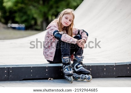 Cute girl roller skater sitting in city park and looking at camera Pretty female preteen kid child posing during rollerskating
