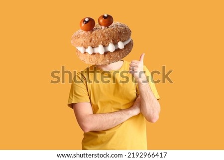 Man with funny monster cookie instead of his head on orange background. Halloween celebration