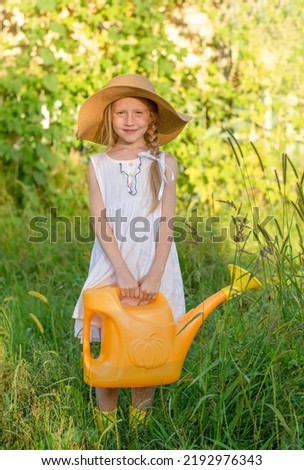 A cute little girl with blonde hair is holding a yellow watering can to water the vegetable garden. Farming and agriculture concept 