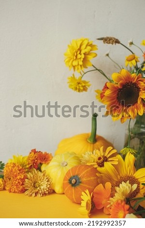 Stylish autumn composition on yellow paper against rustic background. Colorful autumn flowers, pumpkins, pattypan squashes on yellow. Seasons greeting card template with space for text