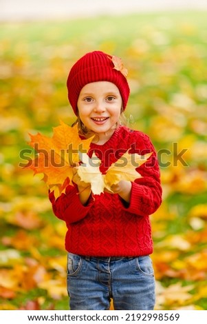 a child is having fun with fallen leaves under a yellow tree on a warm autumn day on a walk. The ground is covered with a carpet of yellow foliage