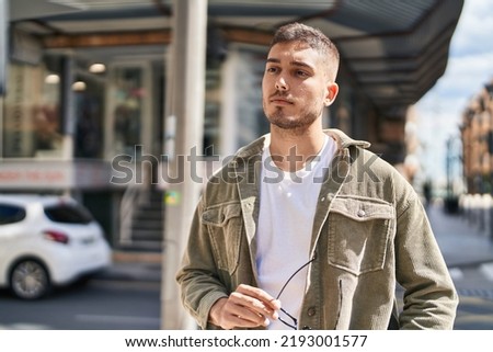 Young hispanic man with relaxed expression standing at street