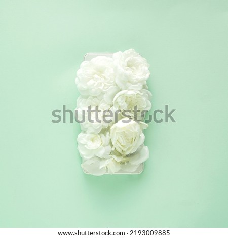 Small white roses on a cell phone screen on pastel green background,flat lay