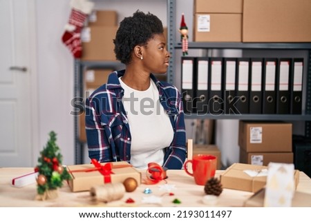 African american woman working at small business doing christmas decoration looking to side, relax profile pose with natural face with confident smile. 