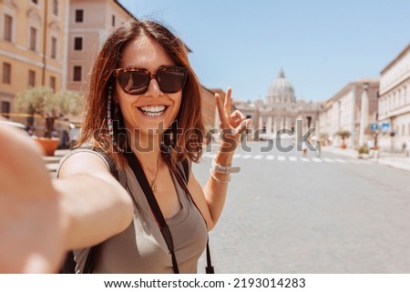 Europe luxury travel vacation tourist in Rome, Italy. Cheerful woman taking selfie photo with phone doing v sign with fingers at Vatican city St Peter's Basilica church. Summer holiday destination.