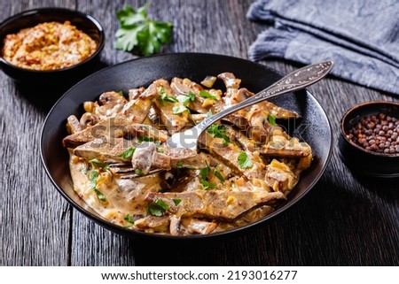 beef liver stroganoff with wholegrain mustard, onion and mushrooms in black bowl on dark wooden table, horizontal view from above Royalty-Free Stock Photo #2193016277
