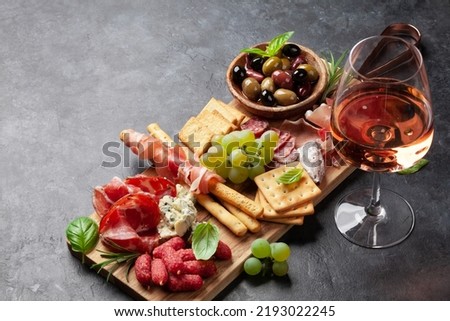 Antipasto board with prosciutto, salami, crackers, cheese, nuts, olives and rose wine. With copy space Royalty-Free Stock Photo #2193022245